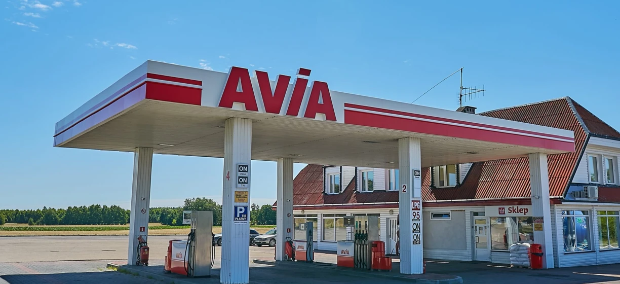 Reflection of a filling station in an automotive mirror with AVIA brand. Fuel dispenser and gasoline available. Rear-view mirror shows the AVIA logo.